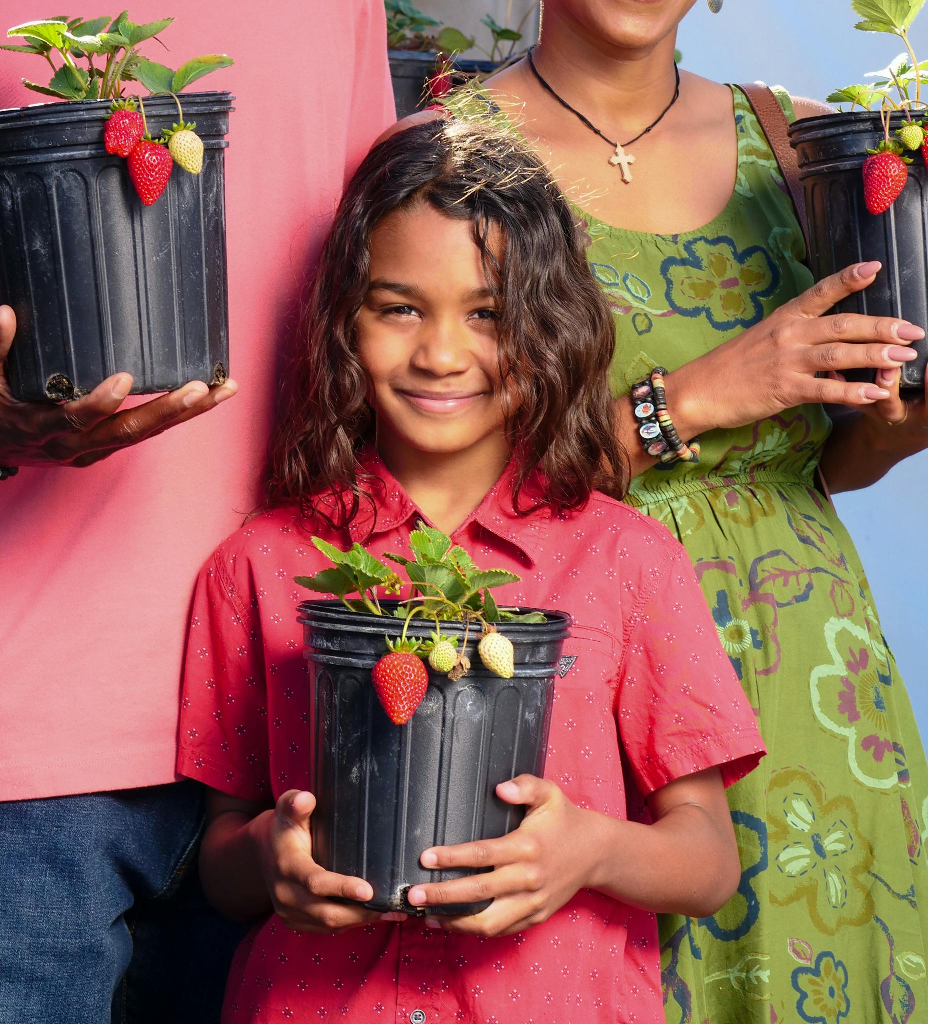 A family joyfully holding strawberry plants, symbolizing organic farming connection.