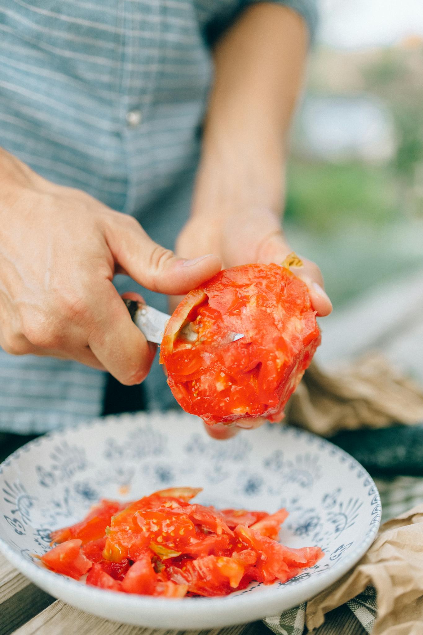 Close-up of a man slicing juicy red tomatoes over a decorative plate outdoors.